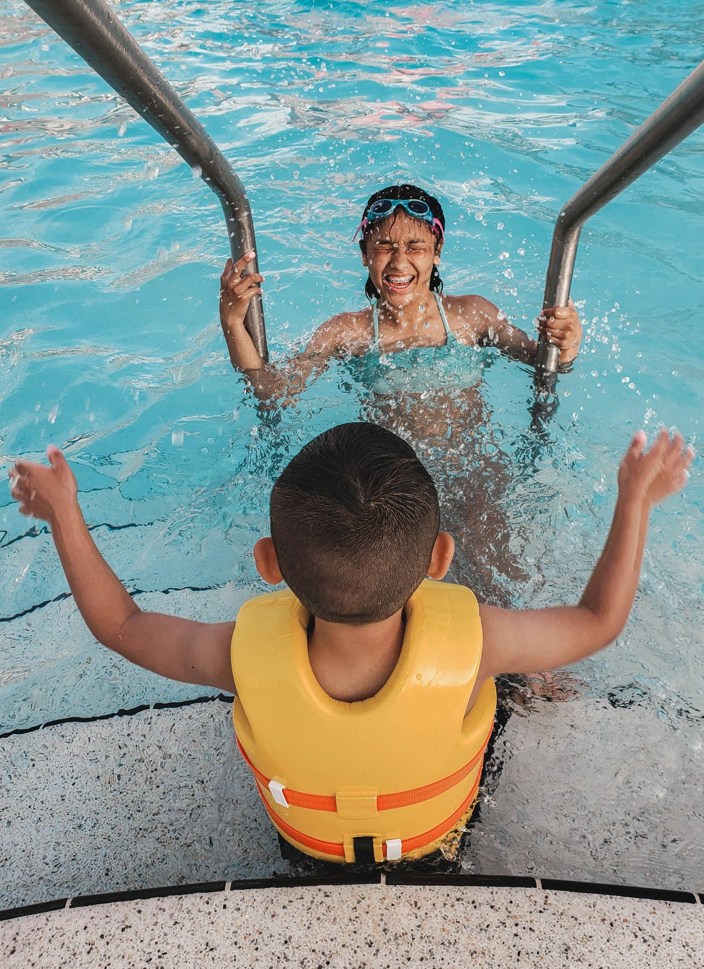 Duas crianças a sair da piscina pela escada, a rir