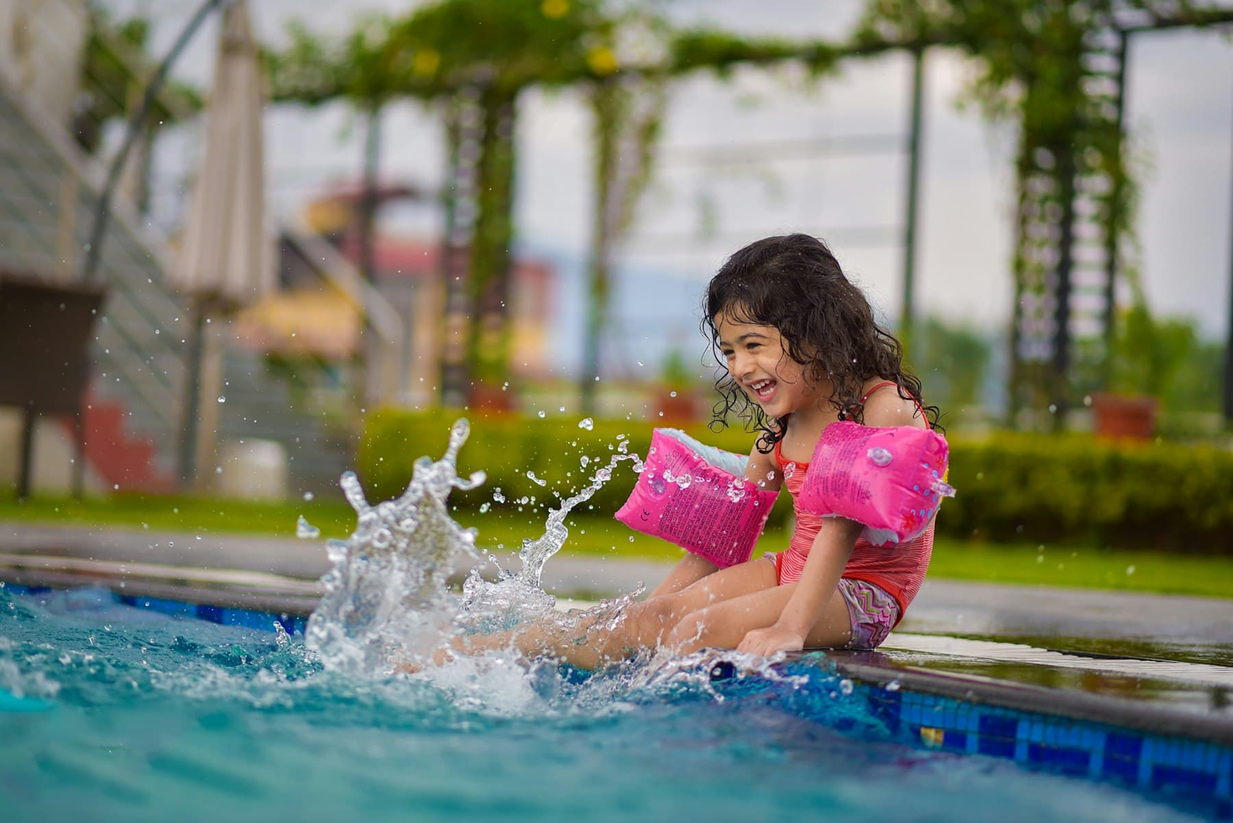 Menina com braçadeiras a salpicar água na borda da piscina